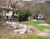Neasfaltirani del stare poti, ki vodi do hiše in mlina Pavličevih (v ozadju), še vedno prekriva kup kamenja  Foto: Ilona Dolenc